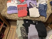 Photo showing various folded sweaters, hoodies, and pants arranged on a patterned couch and floor