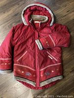 Photo of a red Inuk winter coat in medium size featuring fur-lined hood and cuffs, embroidery, and zippered pockets.