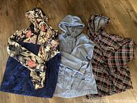 Three ladies summer coats laid out flat: a floral patterned coat, a light gray coat, and a plaid Firefly coat.
