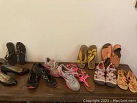Many pairs of ladies shoes and sandals, ten pairs total, displayed on a shelf, including various styles and colors such as black, pink, and orange.