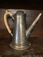 Silver on copper coffee pot with wooden handle shown against a dark wood background, angled side view
