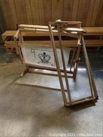 Wooden adjustable cross stitch frame with a fabric showing a crown design, photo taken to display the main cross stitch frame item in lot.