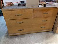 Front angled view of the wooden dresser with six drawers and metal handles, showing the overall structure and condition including worn and stained surfaces.