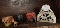 Front view of five elephant items on wooden shelf: planter, two figurines, decorative carved piece, and the clock