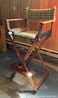 Side angled view showing the folding wooden frame, footrest, and geometric cross-stitched fabric seat and backrest.