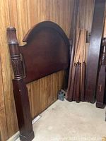 Four poster bed headboard and posts with carved details leaning against wall, disassembled parts stacked nearby.