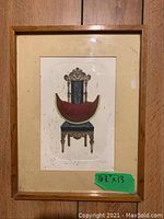 Frontal view of signed artwork print showcasing a detailed antique chair with a red crescent shape, mounted in a splattered wooden frame.