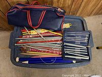 Top view of plastic bin with multiple knitting needles of various sizes and materials including wood and metal. Also multiple crochet hooks in a zippered case and a navy blue storage bag.