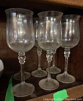 Six identical clear glass votive holders in a row, shown on a shelf with visible decorative stems and circular bases.