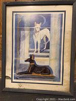 Framed art print showing two Egyptian dogs in a stylized design with some water damage to the mat and some dirt marks near the lower left edge.