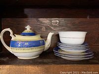 Full view of porcelain teapot, bowl, saucers and plates on a wooden shelf