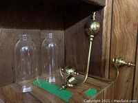 Two vintage brass wall sconces with curved arms and round bases placed on wood background, alongside two clear cylindrical glass shades. A Sharpie pen placed in front for size reference.