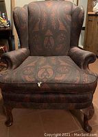 Front view of wing back chair showing patterned fabric upholstery with visible damage on seat cushion