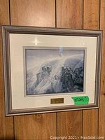 Framed picture of wolf on a snowy cliff hanging on wooden paneling wall, showing entire frame and details of size sticker and plaque.