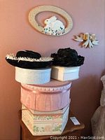 Stack of four vintage-style hat boxes with two black hats on top, on pink wall background.
