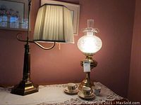 Two bedroom lamps, one with a beige pleated lampshade and one vintage-style etched frosted glass lamp, along with three teacups and two saucers.