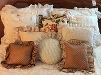 Multiple bedroom pillows arranged showing various sizes and designs including ruffled, embroidered, floral, and textured styles