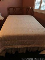 Full view of bed made up with quilted duvet on mattress and decorative bed skirt visible.