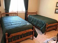 Two wooden twin beds arranged parallel to each other in a bedroom, both with green duvets covering mattresses.