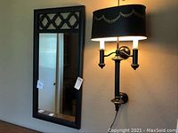 Full view of the tall mirror and black wall lamp mounted on the wall.