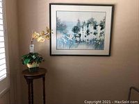 Framed print hanging on wall above wooden plant stand featuring artificial orchid arrangement.