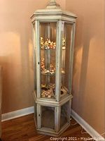 Full view of six-sided curio cabinet with antique white finish, glass shelves, and base storage with glass panels.