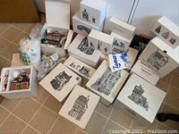Photo of seventeen Dept. 56 Heritage Village building boxes with various village building illustrations on the boxes, arranged on the floor