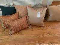Seven decorative pillows arranged on wooden floor showing different angles and patterns.