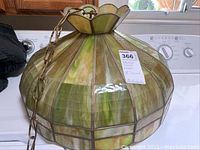 Side view of the stained glass lamp showing its round scalloped petal shape with green and beige stained glass panels and metal framing and chain.