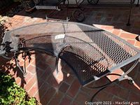 Curved metal bench with lattice pattern seating, angled view showing legs and structure