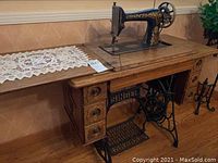 Full side view of the Singer sewing machine mounted in foldout wooden cabinet, showing the machine, foldout tabletop extension, and three ornate drawers.