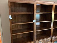 Front view of two tall wooden bookshelf cabinets with open shelves and closed cabinet doors below.
