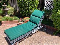 Full view of metal frame outdoor lounger with green cushioned padding on a patio.