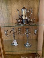 Full tea set and two candle holders on a glass shelf with wooden back.