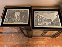 Two framed black and white architectural prints on a wooden cabinet, showing classical buildings and columns with people.