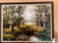Full view of framed oil painting depicting forest and water scene.