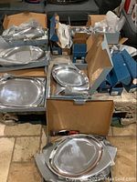 Overview of multiple boxed Nambe Studio platters and bowls arranged on floor