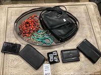 Silver plate tray holding assorted beaded necklaces and multiple black purses and wallets.