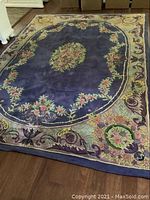 Full view of the large blue floral rug on hardwood floor showing oval center medallion and floral border.