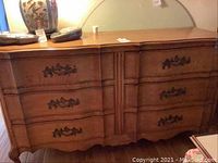 Full front view of the six drawer wooden dresser with a decorative curved front and ornate handles.