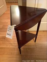 Side angled view of the folded mahogany end table showing the triangular shape and lower shelf.