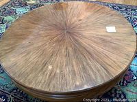 Top view showing circular tabletop with wood veneer in sunburst pattern and minor scratches.