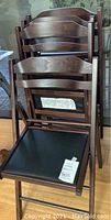 Four wooden folding chairs stacked, showing dark wood finish and black seat padding.