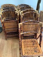 Stack of 19 folding bamboo chairs, showing front views of the seat and backs. Mostly uniform design with two chairs of a different style behind the main stack.