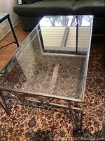 Full view of the rectangular glass-top coffee table showing glass scratches and metal framing.