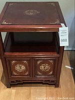 Front view of wooden cabinet showing mother of pearl inlaid doors and open shelf.
