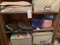 Photo of six various storage containers inside wooden cabinet shelves, including quilted fabric bins, black folded bags, floral box, pink and blue storage bags