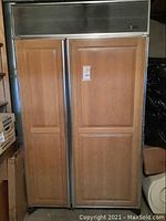 Front view of wood-paneled Sub Zero side-by-side refrigerator showing double door design and vent above doors.