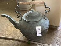 Full view of oversized decorative kettle with wooden handle and ornamental surface.