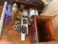 Overview photo showing the colorful camel statue, various small pottery and ceramic decor pieces, a portable heater, a wood trash bin, and gift wrap roll all arranged on a wooden table.